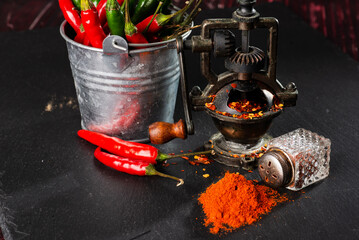 pepper mill,  bunch of red peppers, capsicum and pepper pot on a black table. Close-up. Selective...