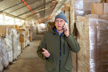 European man warehouse worker talking on phone during workday.