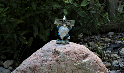 Garden Gnome standing on a stone holding a sign saying: Love Grows Here