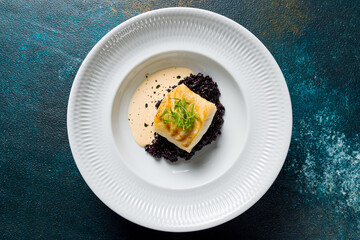 black risotto with fried halibut on a white plate top view