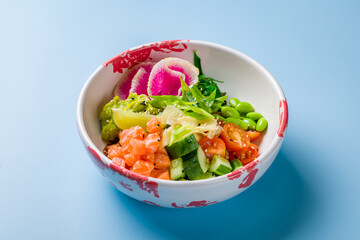 Poke with salmon, rice, cucumbers,tomatoes,edamame,avocado, ginger and chukka on plate on blue background