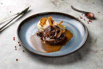 Beef cheeks with mashed potatoes and mushrooms on demiglass sauce on grey table