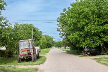 Typical countryside road in the village of Banatsko novo selo, a serbian village of the Banat region of Vojvodina, Serbia, with an old rusted tractor parked, waiting to plough fields....