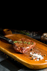 roast beef Steak with salt and pepper on the board on dark stone table vertical