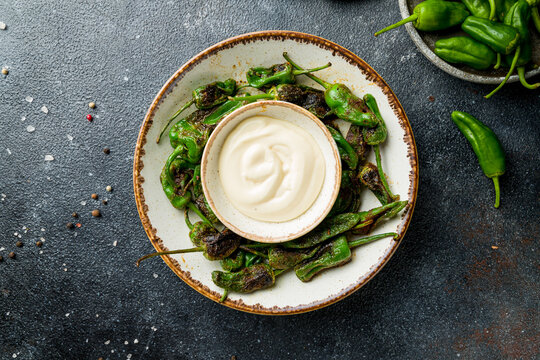grilled green padron peppers with sauce on dark table top view