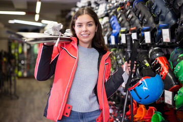 Portrait of young attractive girl choosing modern alpine ski and boots for skiing in sport goods store