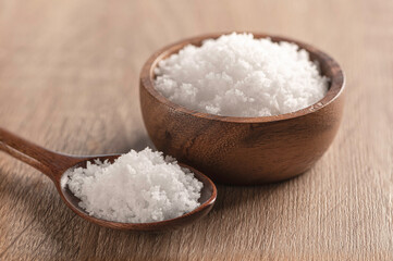 Sea salt in a wooden bowl and spoon on wooden table .
