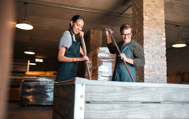 Wine making, production and cellar workers holding press tool to crush, blend and stir open tank for alcohol process. Vintner, factory and winery industry with distillery and manufacturing warehouse