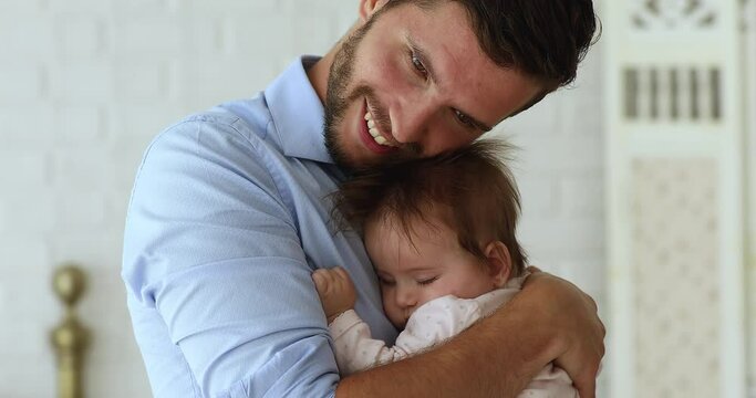 Loving daddy snuggle, cuddle newborn baby girl enjoy sweet moment of tenderness while calming or lulling daughter for day nap at home, close up cropped shot. Happy paternity, true love of dad concept