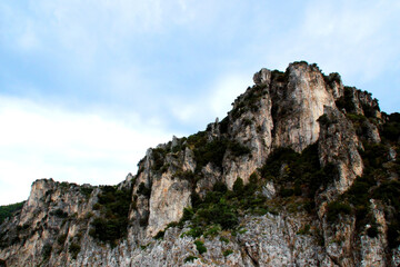 Harsh outlook at a very steep mountain ridge in Amalfi coast punctuated by green vegetation and standing out against a background of hazy azure sky with milky clouds on a summer day