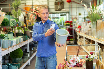 Male shopper scanning qr code on flower pot using smartphone in store
