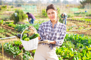 Portrait of happy asian woman showing rich crop of vegetables in kitchen garden on sunny fall day