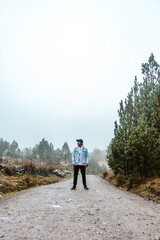 man standing in the middle of a dirt road with cloudy and cold environment