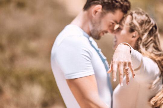 Female hand wearing engagement ring and romantic couple in love after outdoors marriage or proposal. Engaged woman, fiance or smiling, affectionate lovers hugging and embracing in background.