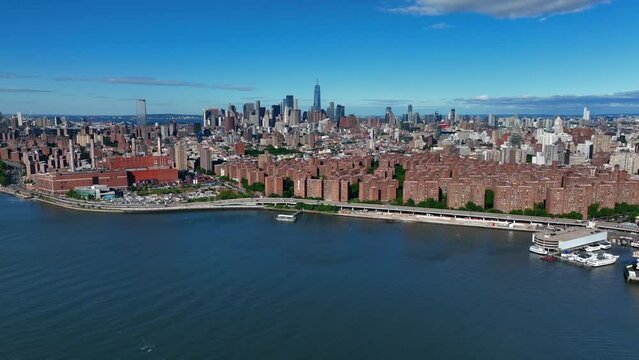 An aerial view of lower Manhattan. Shot from over the East River on a sunny day with blue skies. The stationary drone camera zoom out from the beautiful skyline.