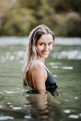 Beautiful smiling blonde girl coming out of the water in a cold river. Vertical