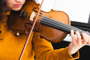 Close up brunette concert woman wearing a yellow sweater, and playing violin by reading sheet music.