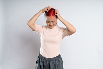 Asian woman scratching her head, with red spot standing isolated on white background.