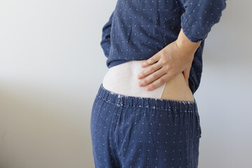 湿布を貼った腰に手をあてる女性の後ろ姿