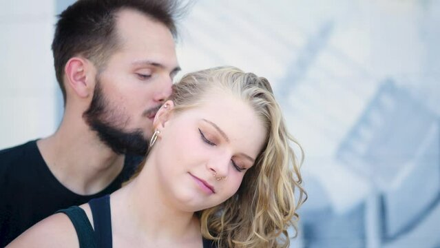 Guy intimately kisses his girlfriend's neck in front of a creative mural. Slow motion.