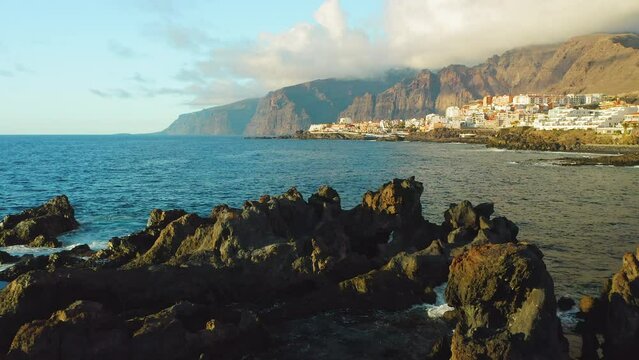 Aerial sunset soft light on rocks. Tenerife, Canary Island, town Puerto de Santiago, Charco el Diablo or natural pool of Devil. Black lava flows, volcanic bizzare stony beach. Scenic spot. Ocean waves