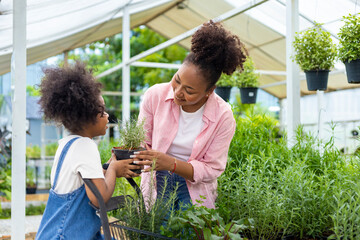 African mother and daughter is choosing vegetable and herb plant from the local garden center nursery with shopping cart full of summer plant for weekend gardening and outdoor concept