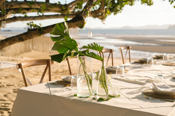 Beautiful table set up for a romantic dinner on the beach with  flowers and candles. Catering for a romantic date, wedding or honeymoon background. Sunset beach dinner. selected focus.