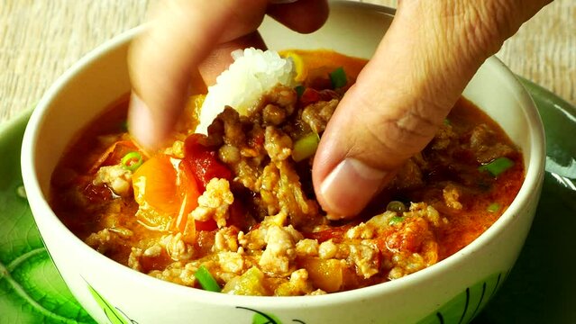 Scooping Nam Prik Ong (Spicy Northern Thai Pork and Tomato) with sticky rice, Thai famous northern food.