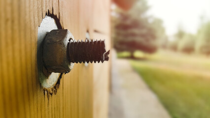A stud with a nut and washer sticks out of a wooden post of a frame house.