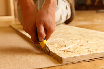 Close-up on the hands of a Carpenter who cuts fiberboard with a mounting knife using OSB.