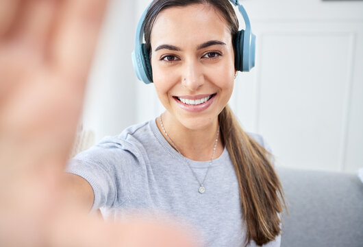 Portrait of happy woman take selfie and smile with headphones while listening to music in the living room. Young beautiful lady streaming a podcast at home and relax in lounge and express happiness