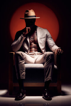Silhouette of mysterious man hiding a secret in the dark sitting on a chair against a red light studio background. Trendy, fashion and style African American model wearing a stylish suit