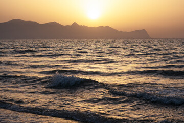 Sunset on island of Sicily, Italy.Waves against the background of the setting sun. Silhouette of mountains in background. Relax, evening on vacation.