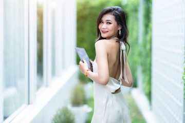 Fototapeta premium beautiful asian freelance Success people business woman fashion model in summer white sleeveless dress using casual working with tablet for browsing internet, chatting and blogging in coffee shop.