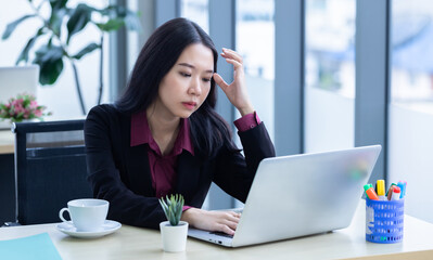 Upset thoughtful Young Asian business woman stress in the workplace working with laptop computer of...