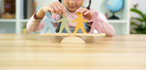 Unidentified little girl is trying to balance the people model on the wooden scale, concept of...