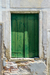 Green window on cracked concrete wall overlooking red bricks