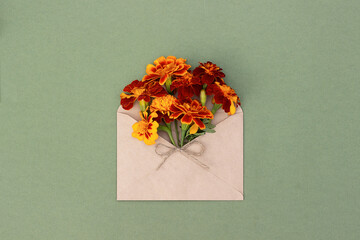 Orange flowers in craft envelope on green background. Top view Flat lay. Summer or autumn minimal...