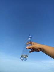 Bottle of mineral water. Person showing transparent bottle with half of water in hand against blue sky background. Copy space. Healthy lifestyle concept. Recycle plastic bottle. Portrait composition.