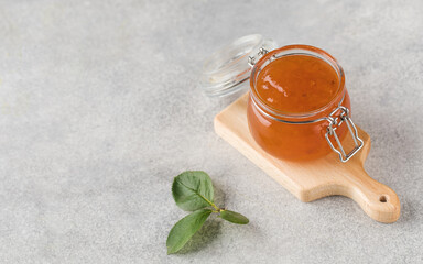 Glass jar with fruity orange jam on a grey background. Fruit preservation.
