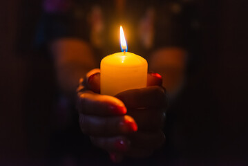 Candle in female hands on black dark background.Prayers candle in hands.