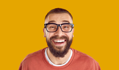 Studio portrait of happy man in glasses. Closeup headshot of cheerful funny bearded nerdy young man wearing eyeglasses looking at camera, smiling and laughing isolated on yellow orange background - obrazy, fototapety, plakaty