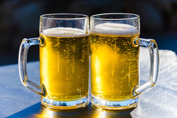 Two glasses of light beer on a table sunset outdoors.Summertime.Closeup.