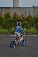 Fototapeta premium Bandung 20 August 2022 - Potrait of young boy playing with his tricycle in the dusk