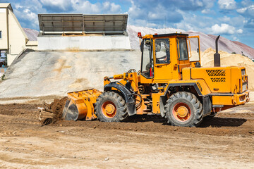 Fototapeta na wymiar A large front loader pours sand into a pile at a construction site. Transportation of bulk materials. Construction equipment. Bulk cargo transportation. Excavation.