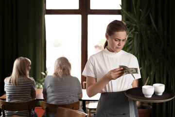 disgruntled female waiter holding serving tray in restaurant with bad tips