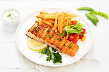 Salmon steak with vegetables and fries on light background.