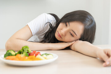 Obraz na płótnie Canvas Diet in bored face, unhappy beautiful asian young woman on dieting, looking at salad plate on table, dislike or tired with eat fresh vegetables. Nutritionist of healthy, nutrition of weight loss.