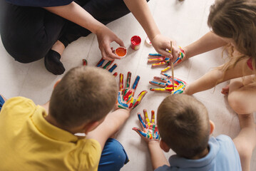 teacher works with children according to the Montessori method and paints their hands. Kindergarten teacher therapy session with children with autism spectrum disorder. - obrazy, fototapety, plakaty