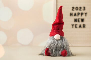  Christmas gnome with a sign with the text 2023 Happy New Year on a background with bokeh and...